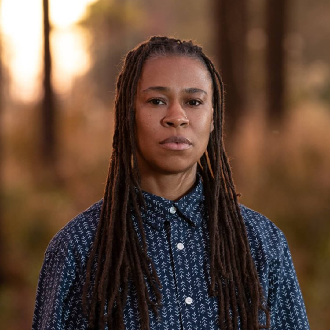 Black trans masculine person with long back locs and blue button down.